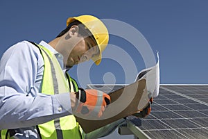 Maintenance Worker Looking At Clipboard Near Solar Panels