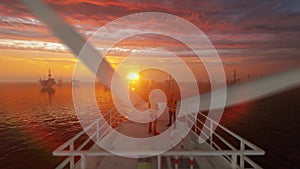 Maintenance worker on top of a offshore wind turbine with oil rigs against sunrise