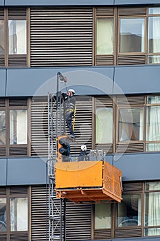 Maintenance workers on a hanging cradle or lifting platform carrying out repair work on the facade of a modern multi-storey office