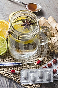 A maison jar with ginger and lemon tea with pills and thermometer on the wooden background