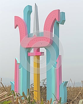 Maize fields backdrop a sculpture of a trident made from reused metal, highlighting sustainability photo