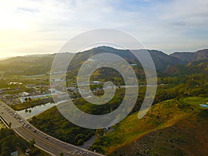 A majestic aerial shot of the lagoon along the mountain ranges with a freeway with cars driving and lush green trees and plants