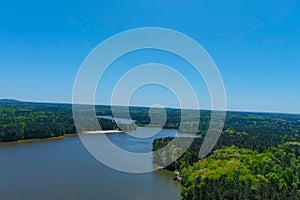 A majestic aerial shot of a rippling lake surrounded by vast miles of lush green trees with a beach on the banks of the lake