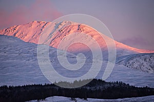 Majestic Alpen Glow hitting mountain peaks in Scottish Highlands during stunning Winter landscape sunrise