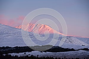 Majestic Alpen Glow hitting mountain peaks in Scottish Highlands during stunning Winter landscape sunrise