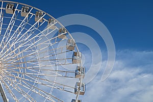 A majestic Ferris wheel stands tall against a cloudy blue sky.
