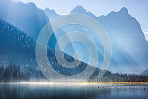 Majestic mountains in bright sunbeams and foggy lake at sunrise