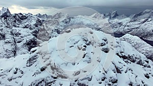 Majestic mountains unfold in an epic aerial shot, draped in snow, battered by strong winds, and set against cloudy skies