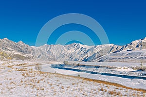 Majestic panoramic view of the valley covered with snow, turquoise river on the background of snow-capped mountains and clear blue
