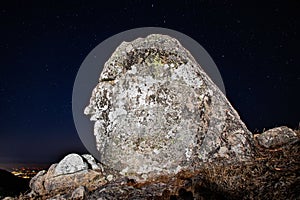 Majestic rock formation standing atop a rocky hillside, illuminated by a star-studded night sky