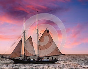 Majestic sailboat is silhouetted against a beautiful blue and pink sunset over the ocean.