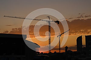 Majestic shot of a silhouette of urban city buildings with construction cranes at golden sunset