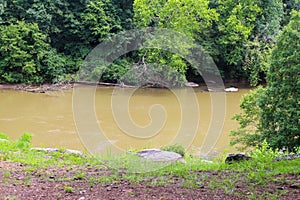 A majestic shot of the silky brown waters of the Chattahoochee river with lush green trees and rocks along the banks of the river