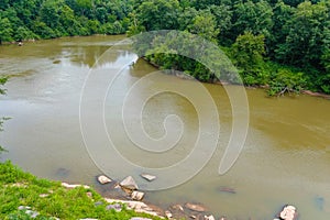 A majestic shot of the silky brown waters of the Chattahoochee river with lush green trees and rocks along the banks of the river