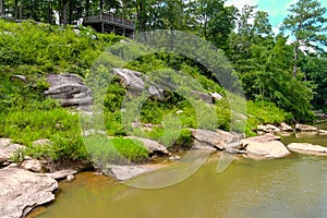 A majestic shot of the silky brown waters of the Chattahoochee river with lush green trees and rocks along the banks of the river