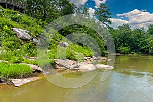 A majestic shot of the silky brown waters of the Chattahoochee river with lush green trees and rocks along the banks of the river