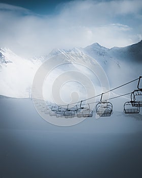Majestic shot of a ski lift against a backdrop of snow-covered mountains shrouded in fog