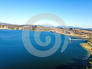 A majestic shot of the still deep blue lake waters, gorgeous mountain ranges and blue sky at Castaic Lake