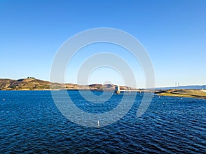 A majestic shot of the still deep blue lake waters, gorgeous mountain ranges and blue sky at Castaic Lake