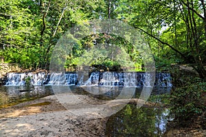 A majestic shot of a waterfall on South Fork Peachtree Creek surrounded by lush green trees reflecting off the water at Lullwater