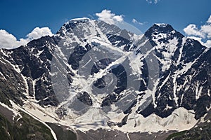 Majestic snow-capped mountains with deep crevasses and glaciers against a blue sky with wispy clouds