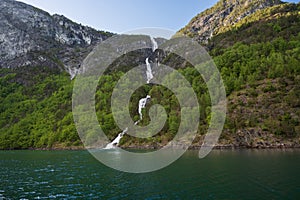 Majestic waterfall, possibly Balai Fossen, cascades down verdant cliffs into the serene Naeroyfjord, part of Sognefjord, Norway, photo