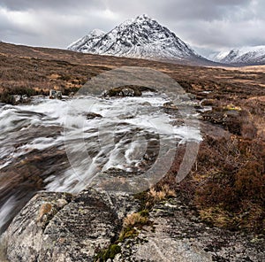 Majestic Winter landscape image of River Etive in foreground with iconic snowcapped Stob Dearg Buachaille Etive Mor mountain in