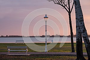 Public bench and streetlamp in front of Palic Lake in Subotica, Serbia, with a green lawn in the foreground, during sunset. photo
