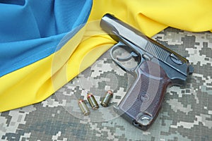 A Makarov pistol with cartridges against the background of a military camouflage pixel and the flag of Ukraine.