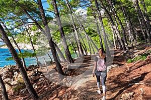 Makarska - Hiker woman on idyllic hiking trail in coniferous forest along tropical stone beach in summer