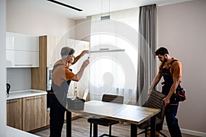 We make it better. Two handymen, workers in uniform fixing, installing light lamp and equipment in the kitchen, using