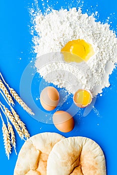 Make bread concept. Flat bread near wheat ears, flour and eggs on blue background top view