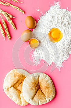 Make bread concept. Flat bread near wheat ears, flour and eggs on pink background top view