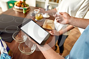 Make a Change. Man checking recipe using tablet pc while woman making smoothie. Vegetarians cooking in the kitchen