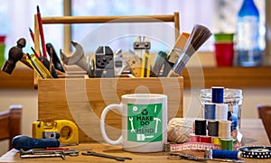 Make do and mend logo on coffee mug surrounded by tools on cafe table top at repair cafÃ©, consumer activism, homespun movement