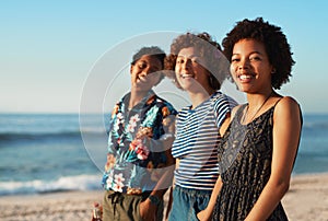 We make each other smile. Portrait of three attractive young women standing together and posing on the beach during the