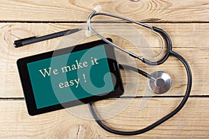 We make it easy! - Workplace of a doctor. Tablet, medical stethoscope, black pen on wooden desk background. Top view