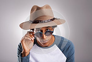 Make a fashion statement...Studio shot of a young man wearing sunglasses and a hat against a gray background.