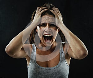 Make it go away. A young woman screaming uncontrollably while isolated on a black background.
