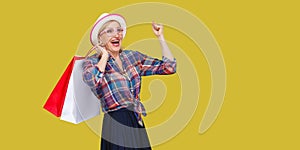 Make a great shopping! Satisfied modern granny in white hat and in checkered shirt holding shopping bags and triumphing with