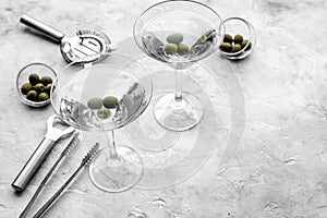 Make martini cocktails. Glass with beverage, olives and utensils on grey stone background top view copyspace