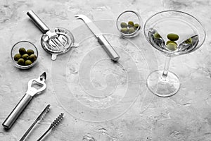 Make martini cocktails. Glass with beverage, olives and utensils on grey stone background top view copyspace