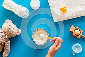 Make mixture for feed baby. Spoon with food in hand near toys and accessories on blue background top view pattern