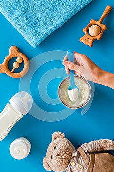 Make mixture for feed baby. Spoon with food in hand near toys and accessories on blue background top view pattern