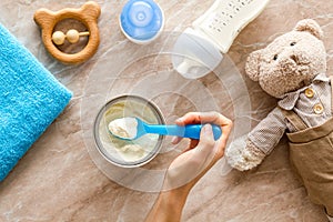 Make mixture for feed baby. Spoon with food in hand near toys and accessories on brown background top view pattern