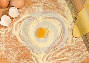 Make a raw dough with flour in the shape of heart and eggs on the wooden table with a rolling pin.