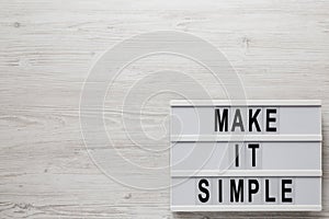 `Make it simple` words on a lightbox on a white wooden background, overhead view. Top view, from above, flat lay. Space for text