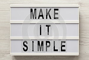 `Make it simple` words on a lightbox on a white wooden background, top view. Overhead, from above, flat lay. Close-up