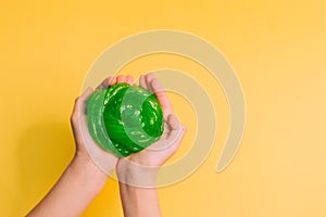 Make a slime green round slimy toy in the hands of children on a yellow background. Copy space, Selective focus
