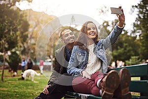 Make sure you get the background in too. a cheerful young couple sitting down on a bench while taking self portraits